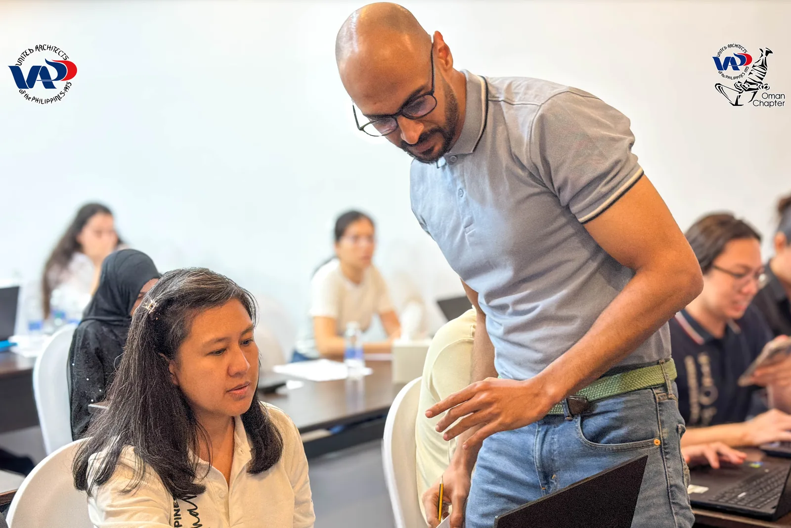 A workshop facilitator helping a participant with a task at her laptop